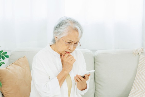 Uma idosa sentada com um celular em uma pose pensativa.