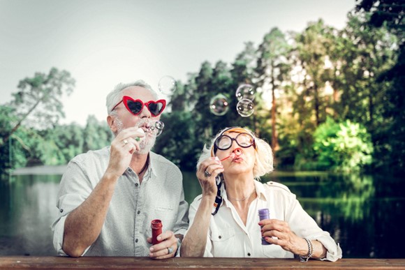 Um casal de idosos em uma ponte de óculos engraçados brincando com bolinhas de sabão.