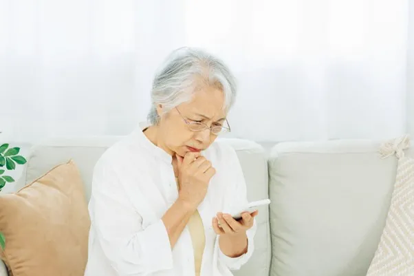 Uma idosa sentada com um celular em uma pose pensativa.