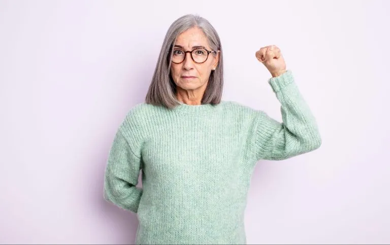 Uma mulher idosa parada com um dos braços levantados em posição de luta